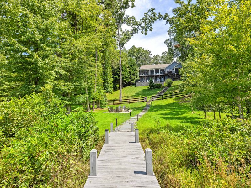 A beautifully designed lakefront home with a screened porch and stone walkway, surrounded by lush greenery for a peaceful retreat.