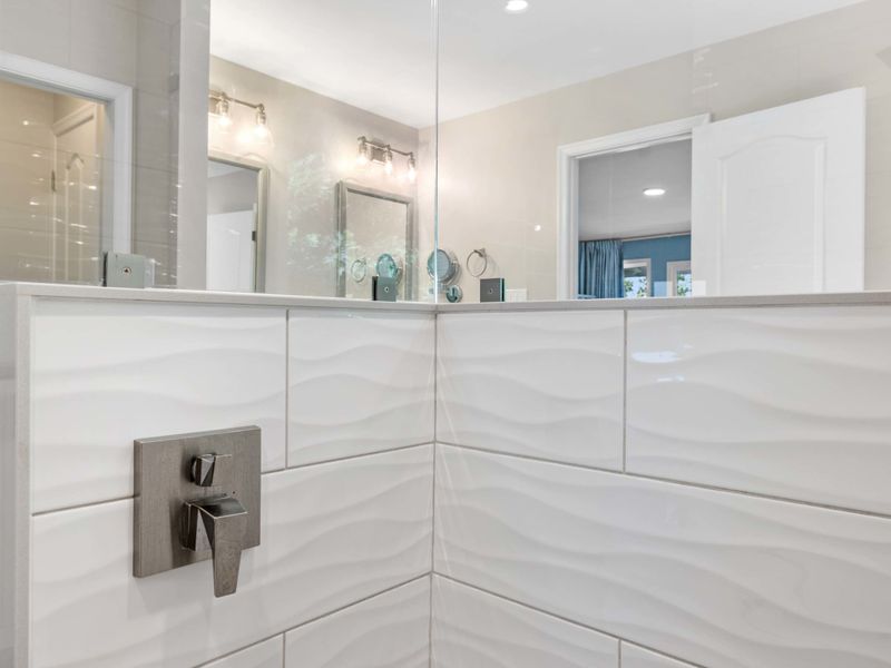 A bright and modern bathroom with a dual-sink vanity, granite countertops, and a view leading to the serene bedroom with lake vistas.