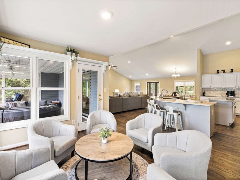 A cozy sitting area with plush chairs and a round table, seamlessly connected to an open kitchen and living space, creating a warm and inviting atmosphere.