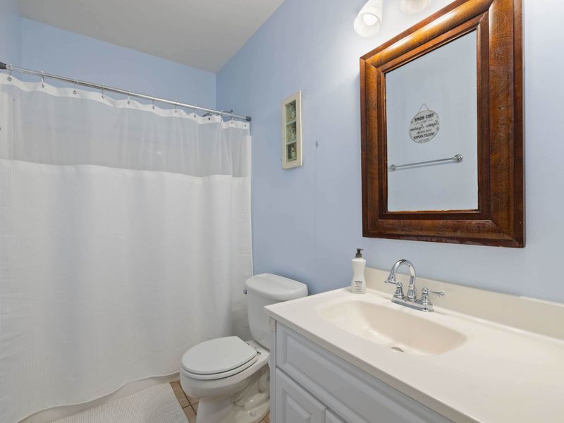 A clean and bright bathroom with a shower and tub combination, a spacious vanity, and a classic wooden mirror for a cozy touch.