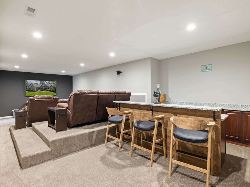 A cozy home theater with tiered seating, plush recliners, and a convenient bar area, perfect for movie nights and entertaining guests.