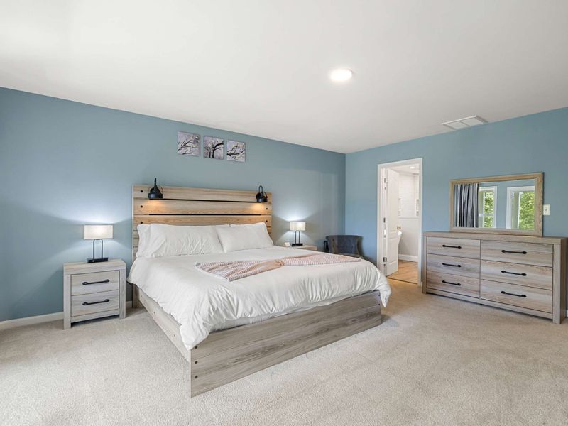 A spacious and serene bedroom with a king-size bed, elegant decor, and large windows opening to a private balcony with lush views.