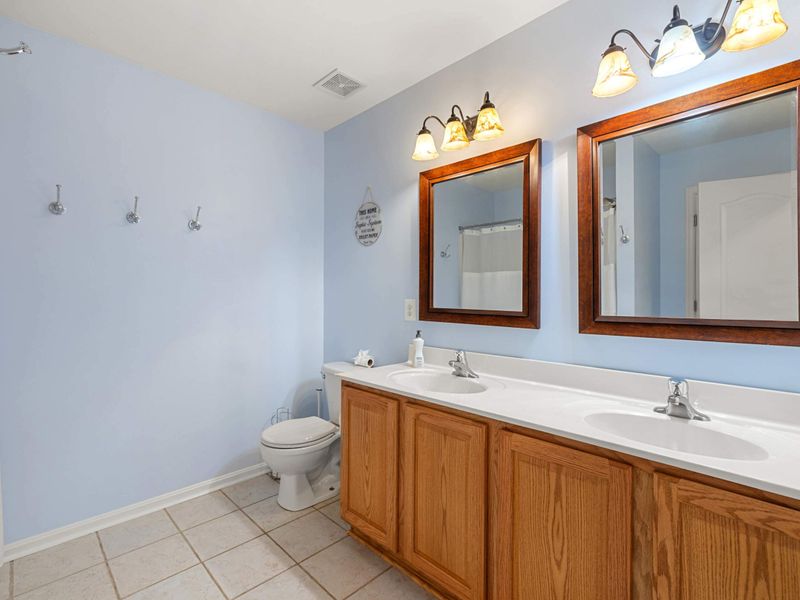 A bright and functional bathroom featuring a dual-sink vanity with wood cabinetry, large mirrors, and a clean, inviting design.