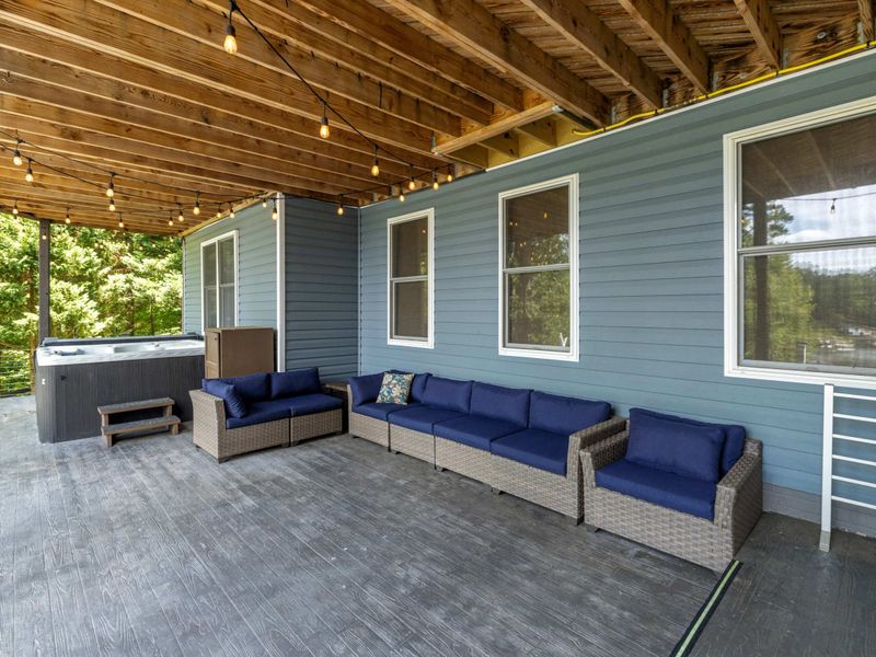 A spacious covered patio with cozy outdoor seating, string lights, and a hot tub, offering a relaxing retreat with scenic views.
