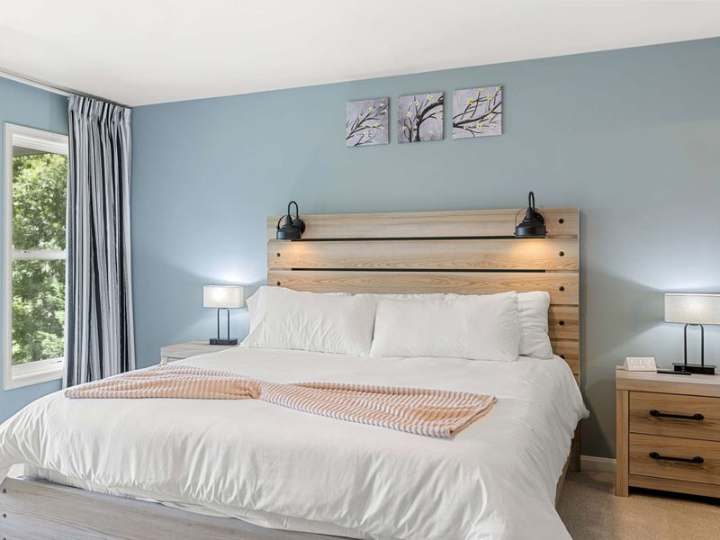 A spacious and serene bedroom with a king-size bed, elegant decor, and large windows opening to a private balcony with lush views.