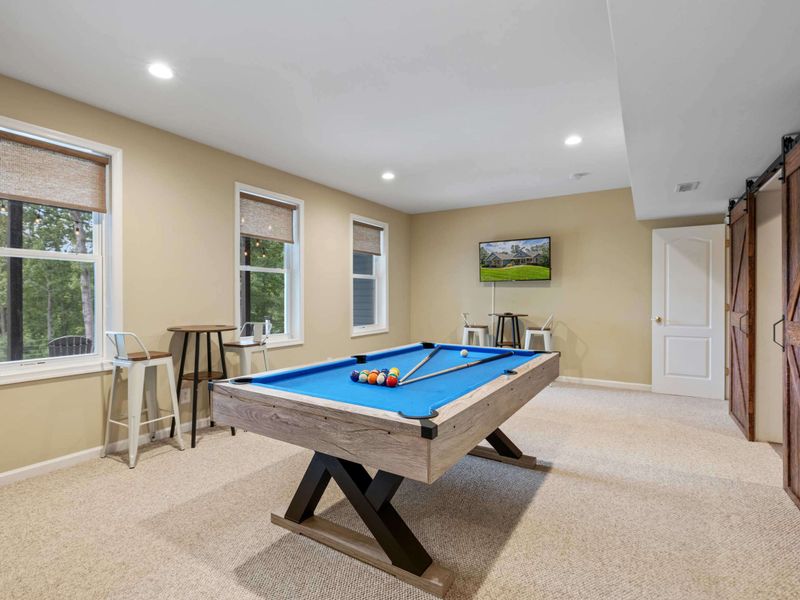 A spacious game room featuring a pool table, cozy seating, and rustic sliding barn doors leading to a home theater, perfect for entertainment and relaxation.