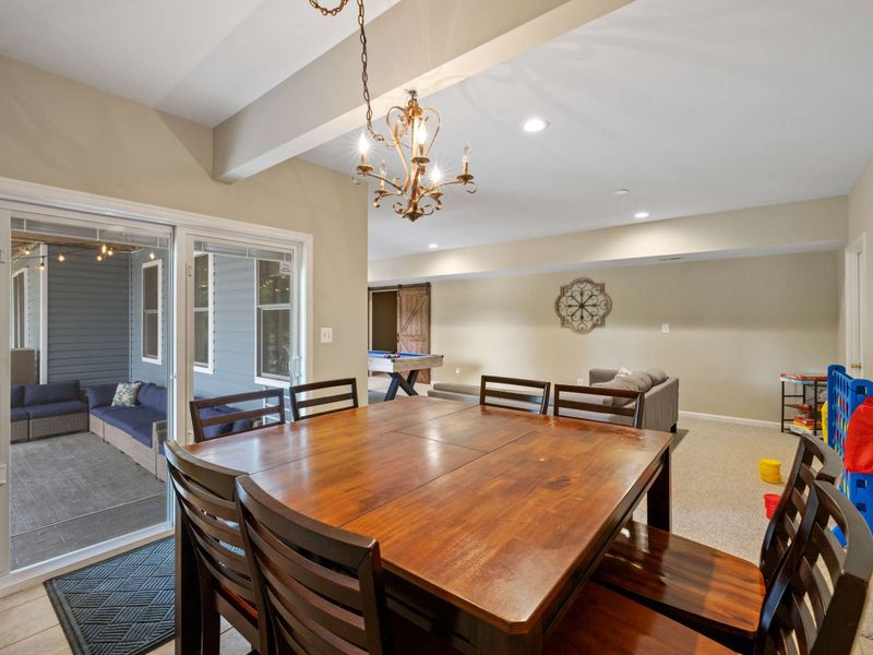 A welcoming dining area with a wooden table, adjacent to a game room and a covered patio, offering versatile spaces for dining and entertainment.