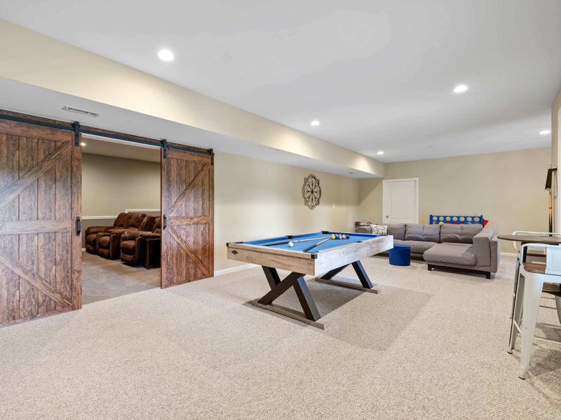 A spacious game room featuring a pool table, cozy seating, and rustic sliding barn doors leading to a home theater, perfect for entertainment and relaxation.