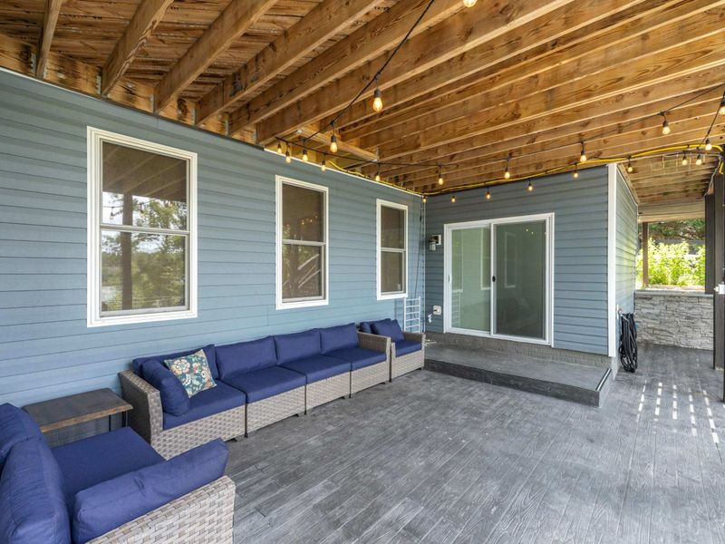 A spacious covered patio with cozy outdoor seating, string lights, and a hot tub, offering a relaxing retreat with scenic views.