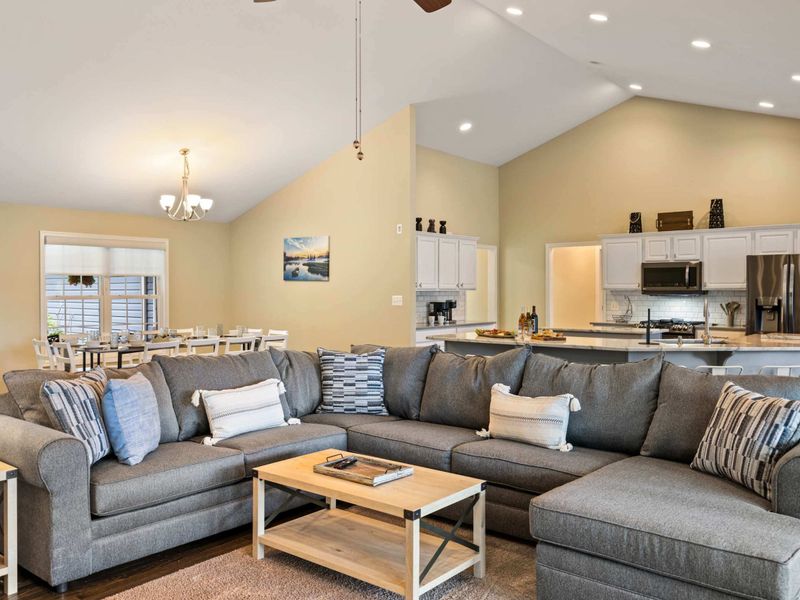 An inviting open-concept living space with a cozy sectional sofa, high ceilings, and a modern kitchen, perfect for gathering and relaxation.