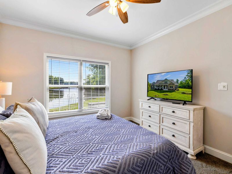 Bedroom - Alternate angle showing the queen bed with a smart TV on a white dresser and tropical ceiling fan.