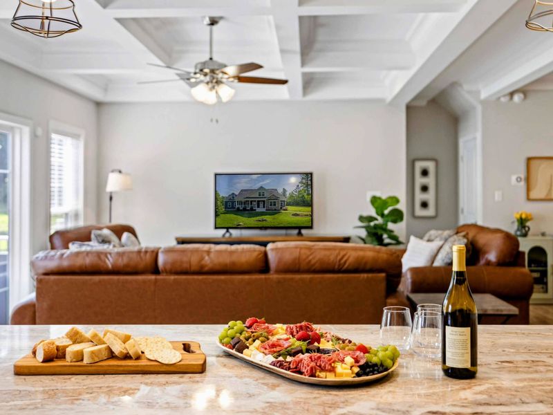 Elegant kitchen island setup with a charcuterie board and wine, overlooking a cozy living room with a TV