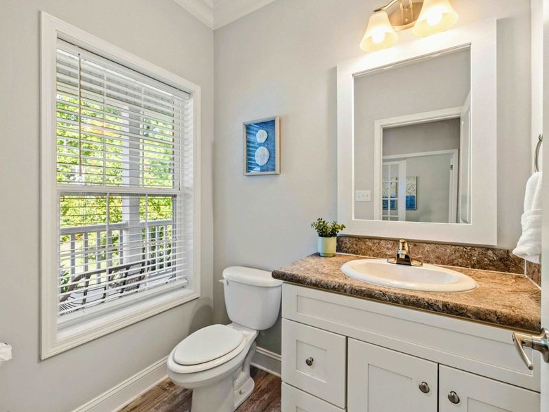 Half Bath - Single granite vanity with coastal art, a window for natural light, and clean white cabinetry.