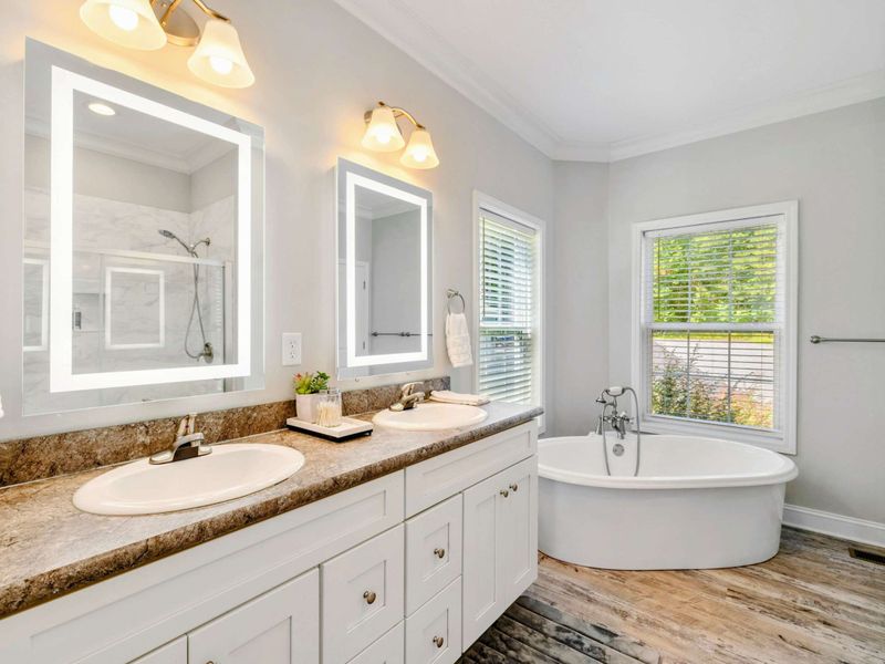 Primary Suite Bathroom - Elegant bathroom with a double vanity, illuminated mirrors, and a relaxing soaking tub