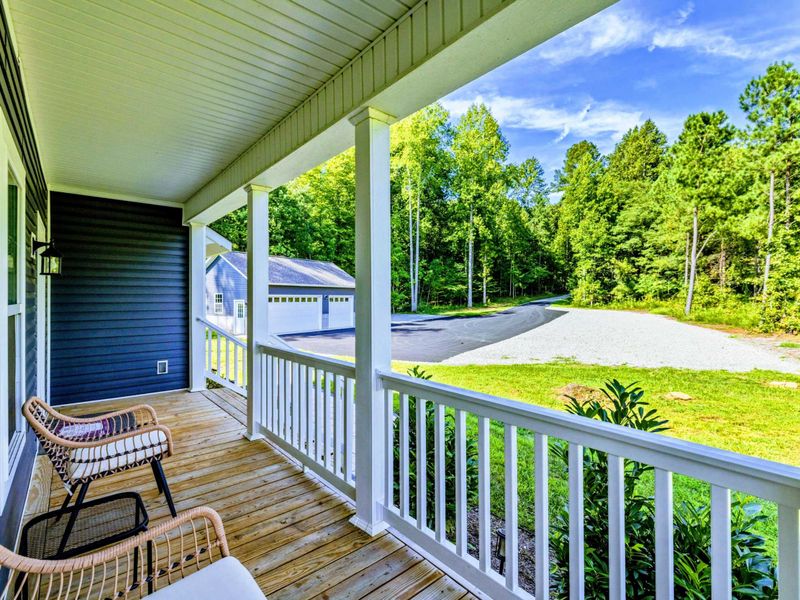 Front Porch - View from the porch looking out over the yard, driveway, and detached garage surrounded by trees.