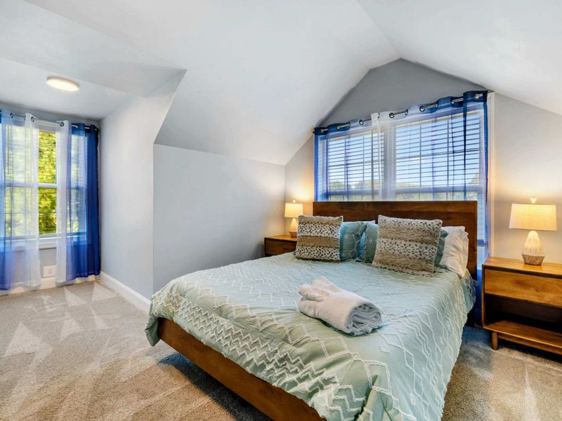 Upper Bedroom - Alternate angle showing the king bed under the dormer peak with blue curtains and natural light.