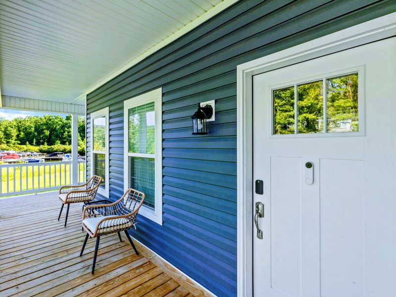 Front Porch - Covered porch with rattan seating chairs, blue siding, a lantern sconce, and views of the lake beyond.