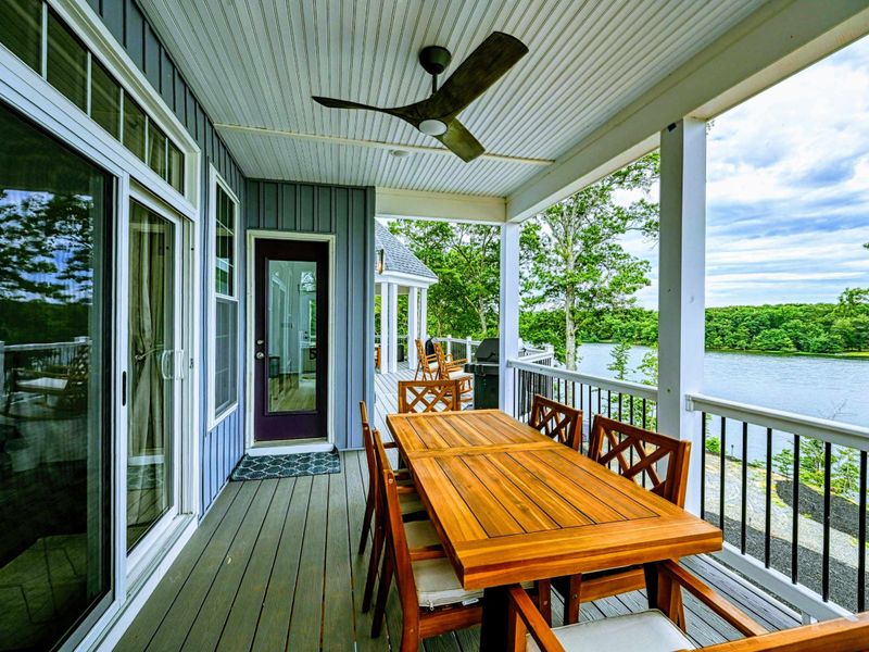 Charming covered deck with a large dining table and ceiling fan, perfect for enjoying meals with a scenic lake view
