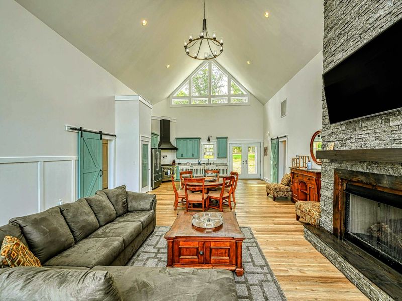 Open-concept living and dining area with high vaulted ceilings, a stone fireplace, and elegant furnishings, offering a warm and inviting space