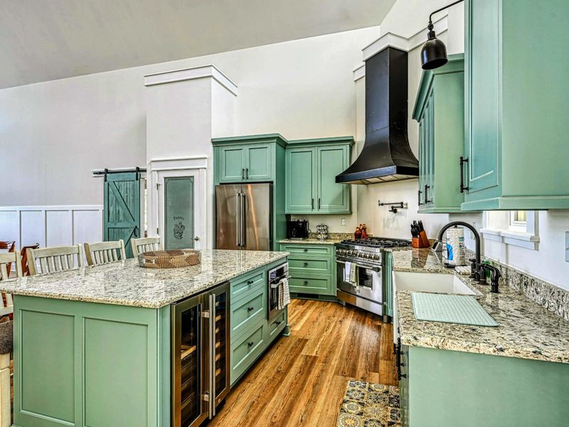 Modern kitchen with a large granite island, wine cooler, and sleek green cabinetry, perfect for preparing and enjoying meals