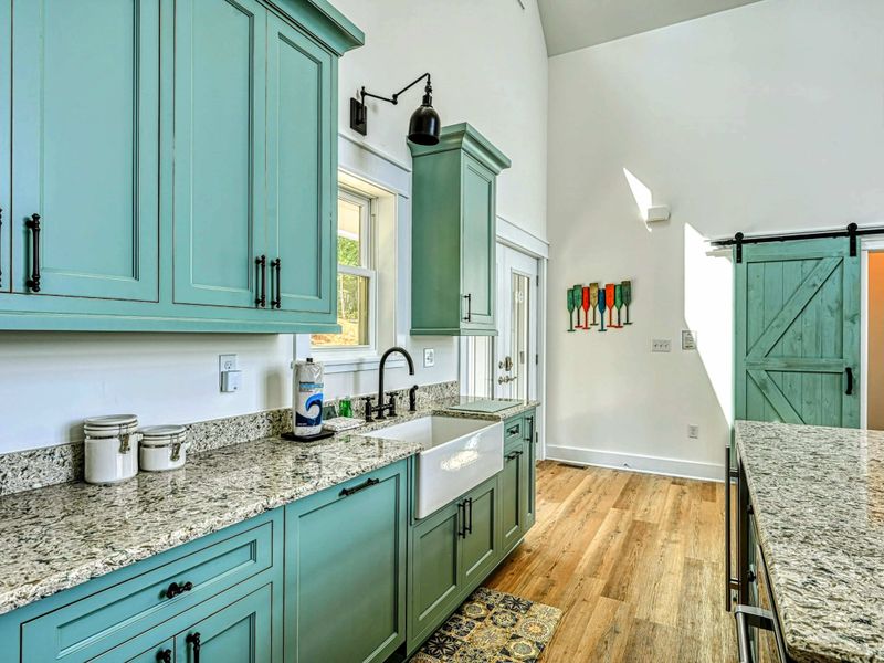 Charming kitchen with a farmhouse sink, stylish green cabinetry, and a sliding barn door, combining modern comfort with rustic elegance
