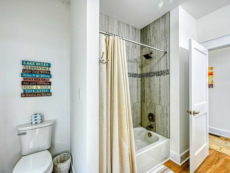 Clean and stylish bathroom with a tiled shower, tub combo, and charming lake-themed decor