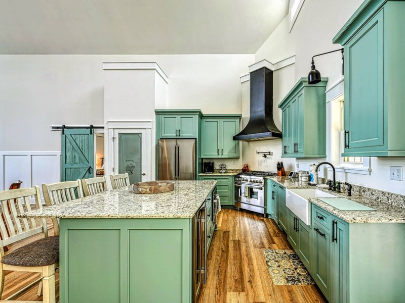 Stylish kitchen featuring a large granite island, farmhouse sink, and modern green cabinets, ideal for culinary enthusiasts