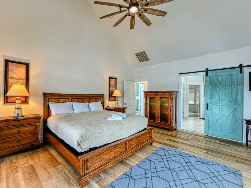 Spacious Primary Bedroom with a rustic wooden bed, vaulted ceilings, and a charming sliding barn door for a touch of farmhouse elegance