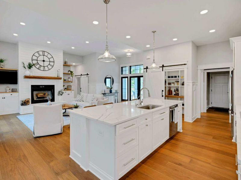 Open-concept kitchen and living area featuring a spacious marble island, modern fixtures, and seamless flow into a cozy, well-lit living room.