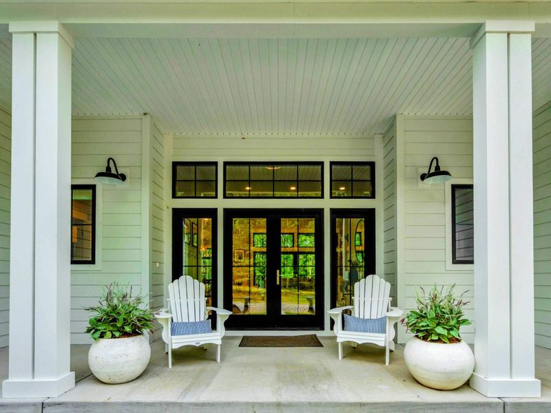 Charming covered entryway featuring Adirondack chairs, elegant lighting, and inviting double doors.