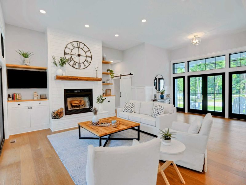 Bright and airy living room featuring a cozy fireplace, stylish furnishings, and large windows for natural light.