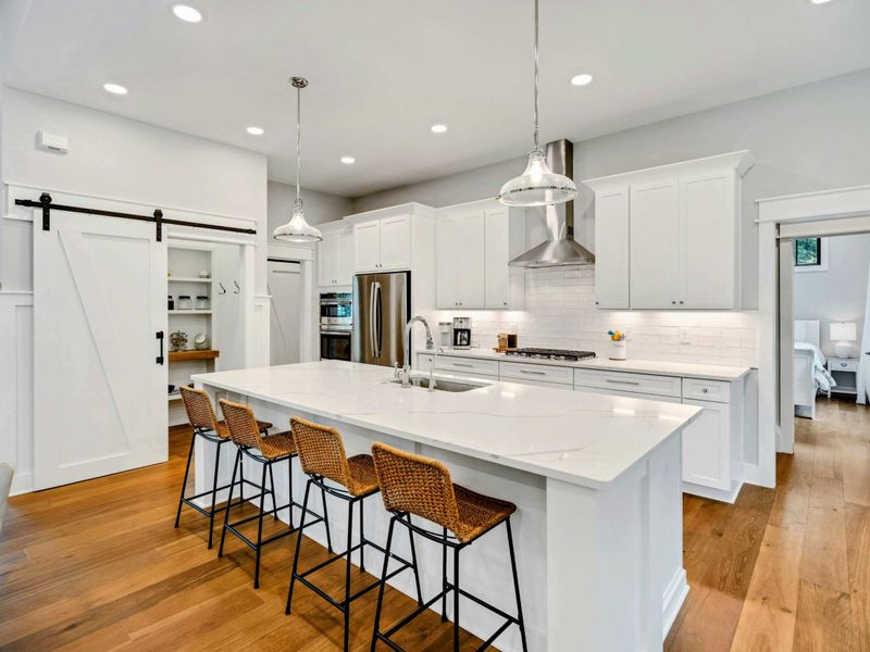 Modern kitchen with a large quartz island, stainless steel appliances, farmhouse-style barn doors, and seating for four.