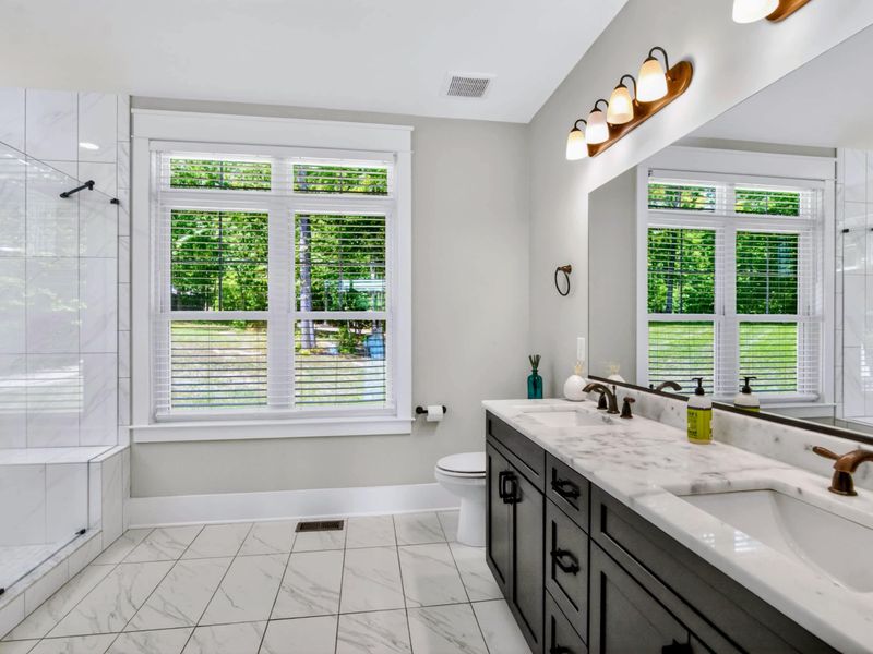 Suite 1 Bath - Marble double vanity, glass walk-in shower, and treetop views from the tub-line windows, more spa than functional.