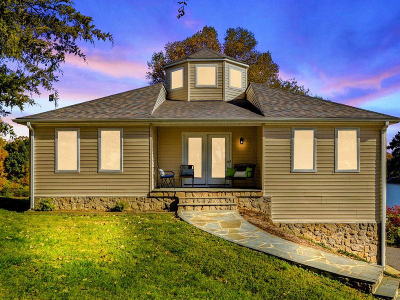 Exterior - Front view of the home at twilight with a cupola, stone accents, a covered porch, and the lake glowing in the background.