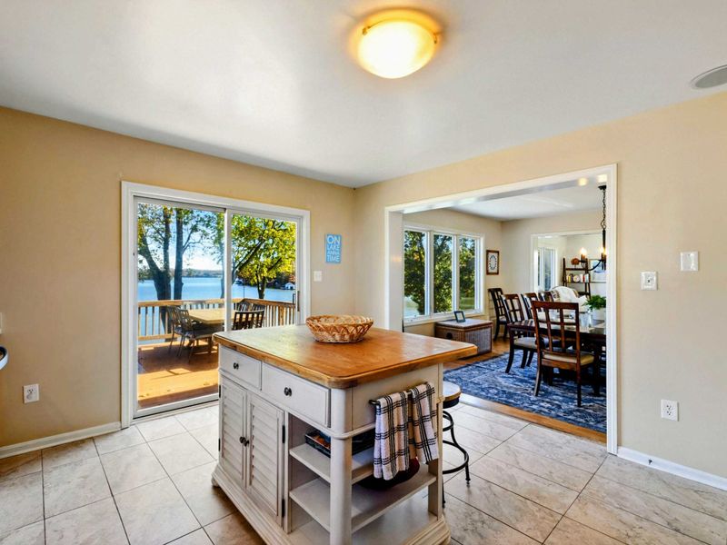 Kitchen - Butcher-block island with white cabinetry, sliding glass doors to the lakefront deck, and views into the dining room.