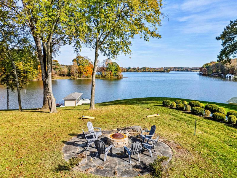 Picturesque fire pit area with Adirondack chairs, set against a beautiful lakeside backdrop