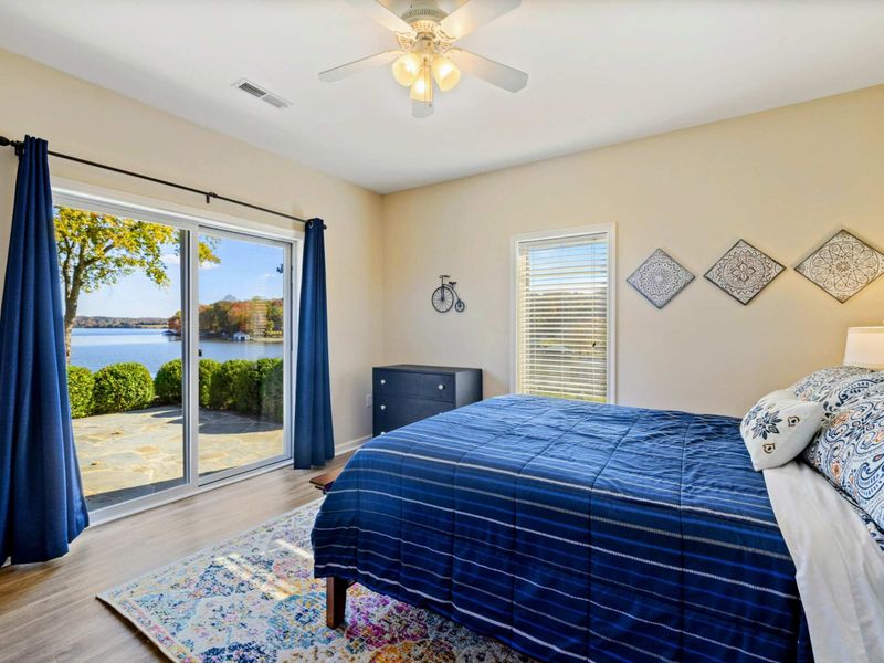 Bedroom - Queen bed with navy blue bedding, decorative tile wall art, sliding glass doors with direct lake views, and a colorful area rug.