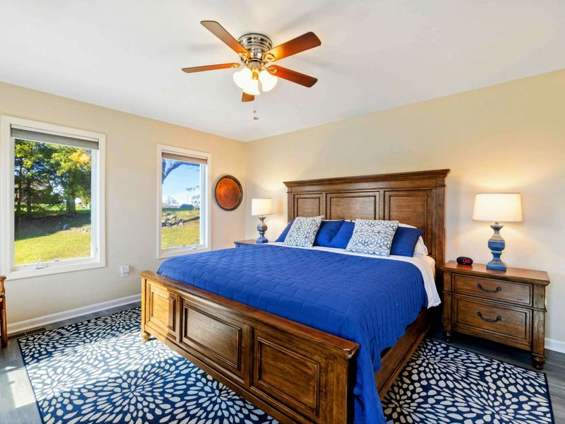 Primary Suite - King bed with rich wood furniture, royal blue bedding, blue floral area rugs, and lake views through corner windows.