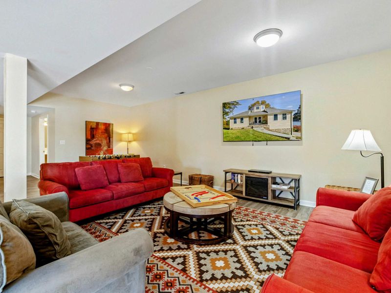 Lower Level Lounge - Alternate angle showing the red sofas, farmhouse canvas, TV, and warm lighting.