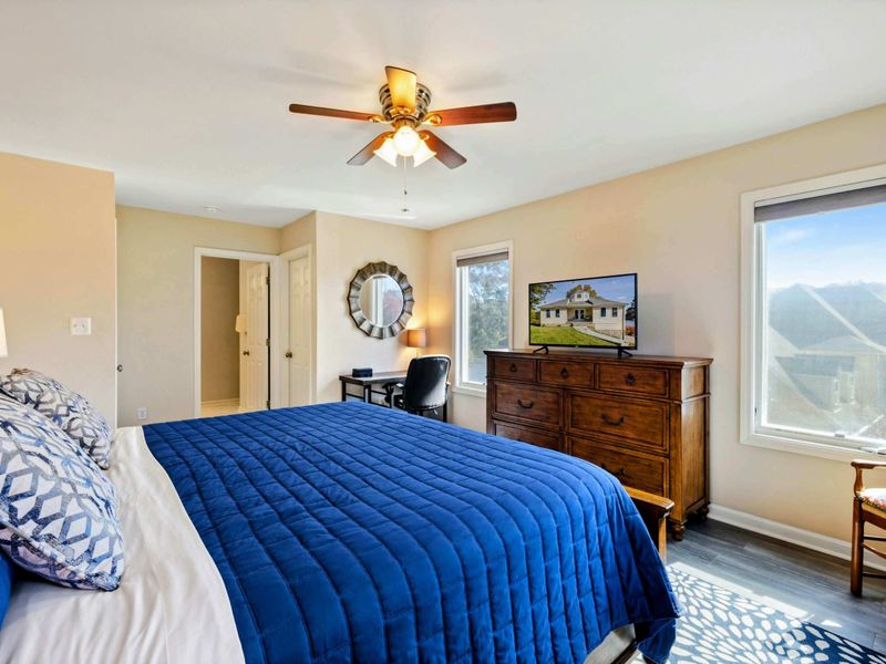 Primary Suite - Alternate angle with the king bed, smart TV on a wood dresser, sunburst mirror, and desk area.