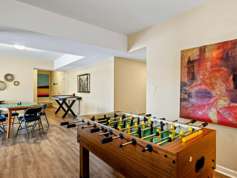 Game Room - Foosball table with a large abstract canvas, poker and air hockey tables, and woven basket wall art beyond.