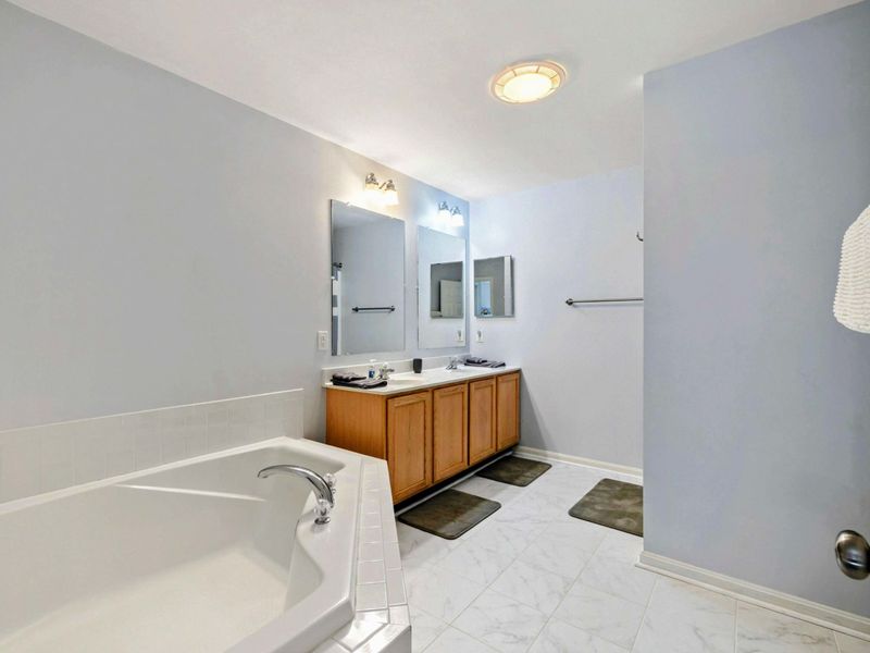 Primary Bathroom - Spacious ensuite with a corner soaking tub, double vanity with oak cabinetry, and soft blue walls.