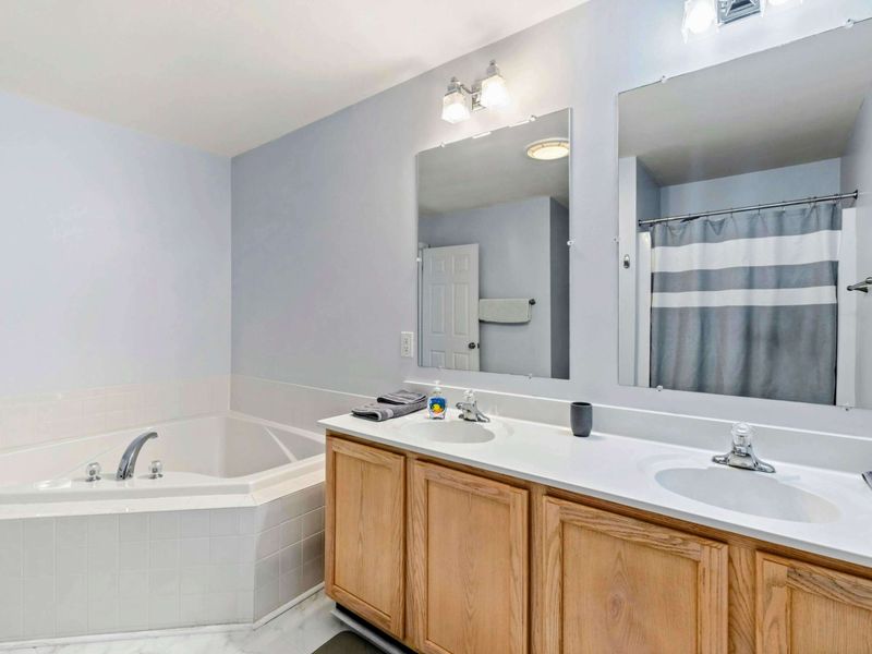 Primary Bathroom - Double vanity with oak cabinetry, large mirror, corner soaking tub, and a striped shower curtain.