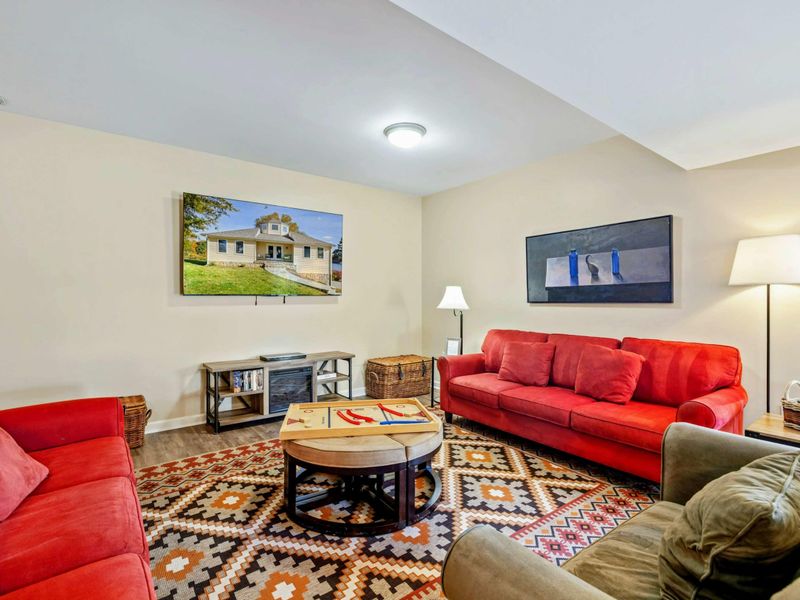 Lower Level Lounge - Red sofas, a gray loveseat, round coffee table with board games, wall-mounted TV, and a bold geometric rug.