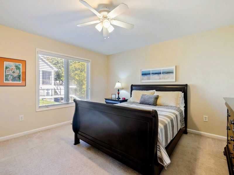 Bedroom - Queen bed with a dark sleigh frame, gray striped bedding, coastal art, and views of the yard through the window.
