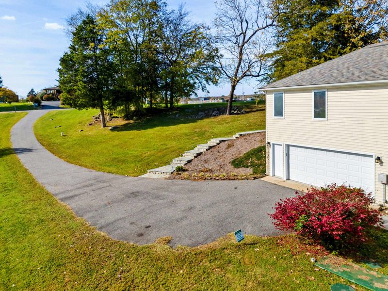 Aerial - View of the driveway and attached garage with the manicured lawn, stone retaining wall, and autumn bushes.
