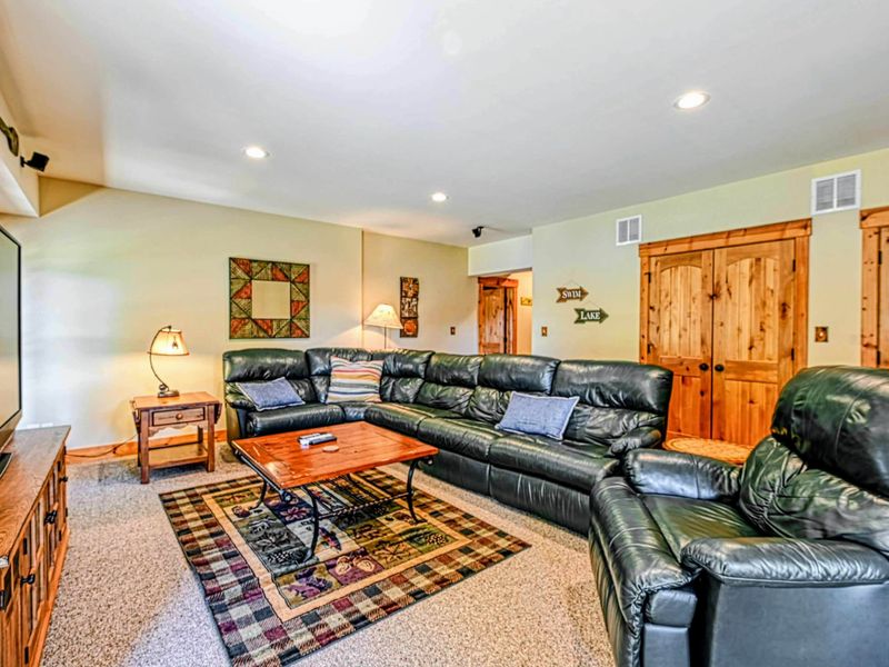 Great Room - Floor-to-ceiling A-frame windows flood the room with natural light while leather seating and a red area rug anchor the space.