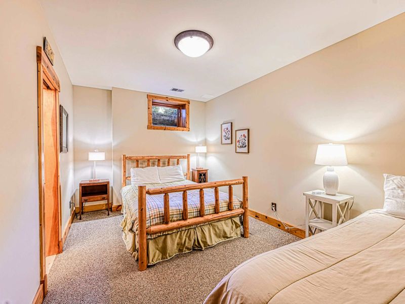 Rest in this cozy bedroom featuring a charming wooden bed frame, an additional twin bed, and soft lighting for a peaceful stay.