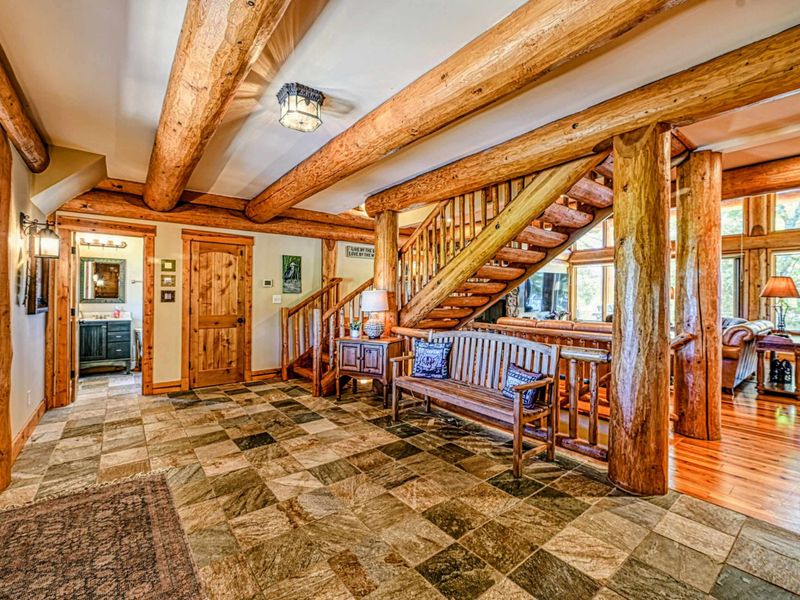 Great Room - Soaring two-story space with a stone fireplace, exposed log beams, loft railing above, and leather seating on hardwood floors.