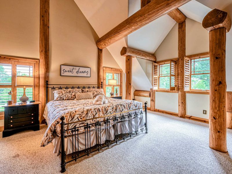 Sleep peacefully in this stunning loft-style bedroom featuring vaulted ceilings, exposed wooden beams, and abundant natural light for a cozy retreat.